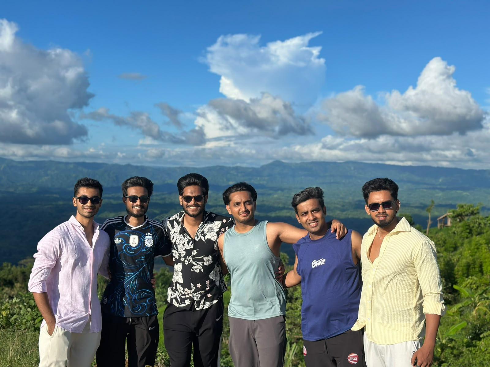 Aehtesham with five friends on a hilltop, green mountains and a wide blue sky behind them